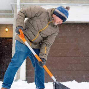 Čovek koristi grejač za vrat dok sklanja sneg ispred svog doma