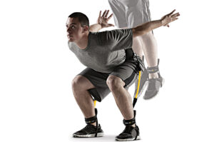 Muškarac koristi Latex Pojas za Skokove za unapređenje skočnosti, prikazan u pozi pripreme za skok sa žutim elastičnim trakama